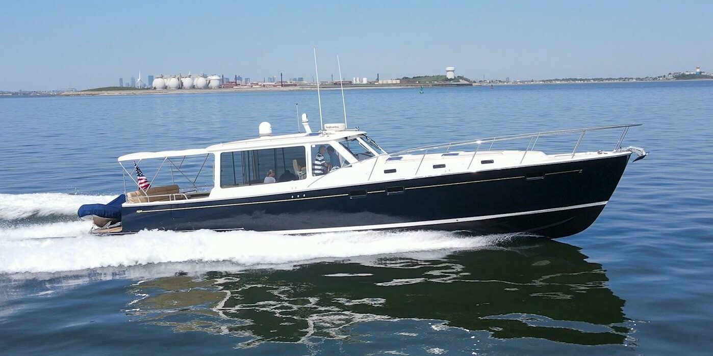 MJM 50z cruising on smooth water from the starboard side with an American flag and tender visible on the stern.