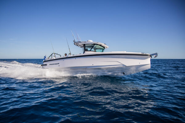 Axopar 29 CCX (Center Console) running through deep blue ocean on starboard side with Finnish flag visible on the stern, under a clear blue sky.