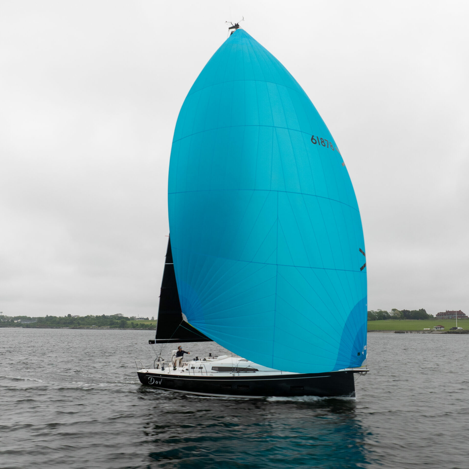 J/40 “Dov” with black and white color scheme sailing off Portsmouth, Rhode Island on a gray day, with a bright light blue spinnaker prominently displayed, one person on deck.