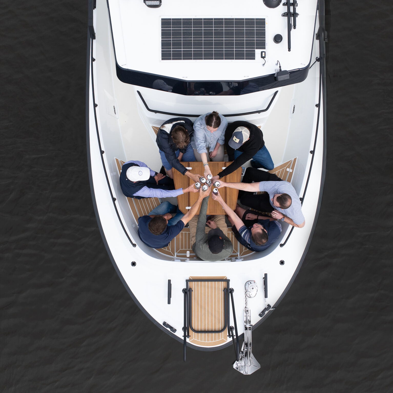 Top-down view of eight people enjoying drinks on the bow seating area of a Targa 32 Outboard on calm waters.