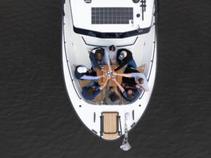 Top-down view of eight people enjoying drinks on the bow seating area of a Targa 32 Outboard on calm waters.