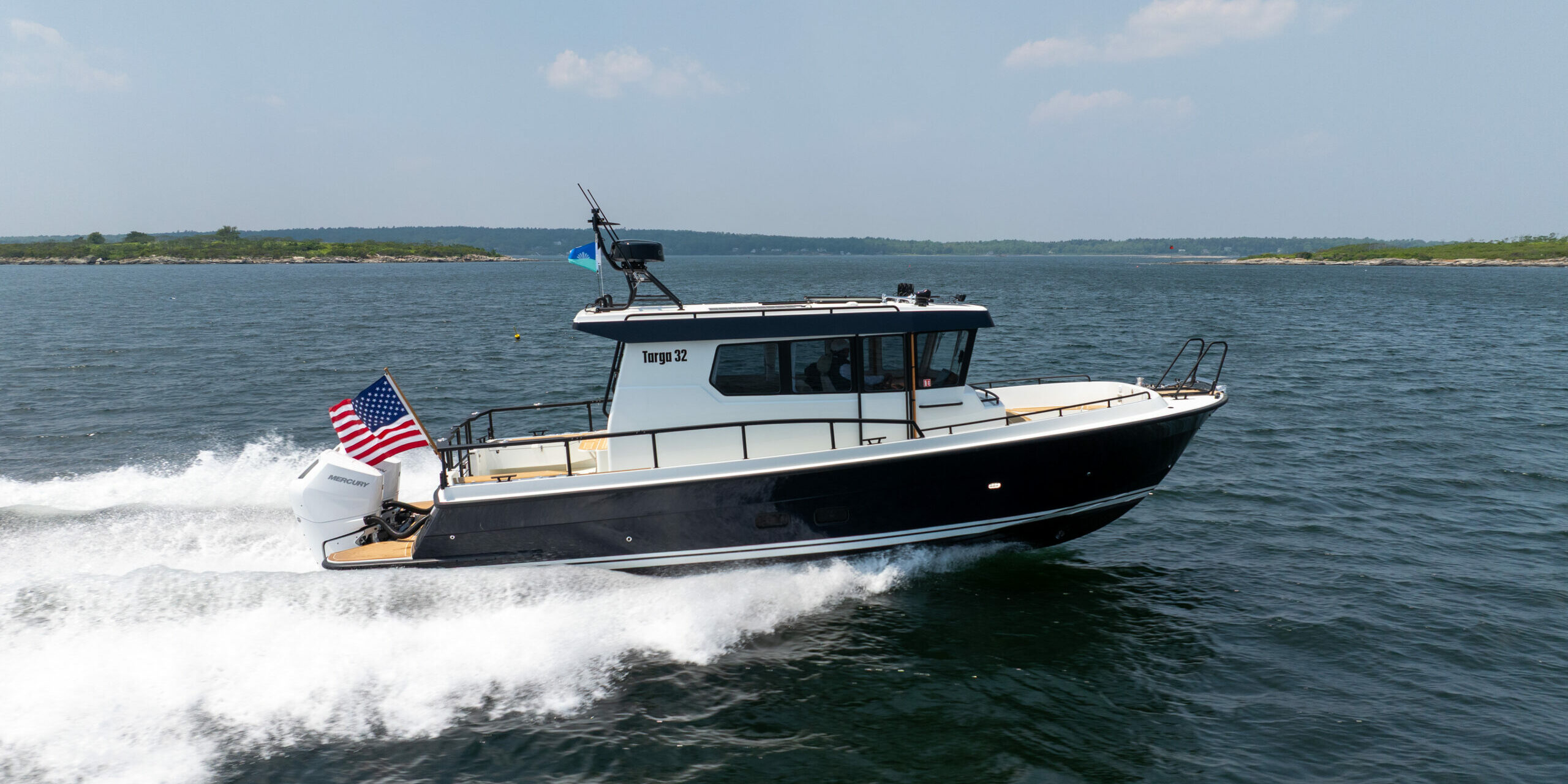Targa 32 Outboard Side View in Casco Bay – East Coast Yacht Sales Side view of a Targa 32 Outboard cruising in Casco Bay, Maine, showing the full boat, twin Mercury 350 outboards, and an American flag flying from the stern.