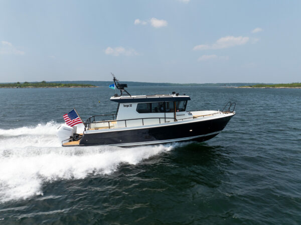 Side view of a Targa 32 Outboard cruising in Casco Bay, Maine, showing the full boat, twin Mercury 350 outboards, and an American flag flying from the stern.