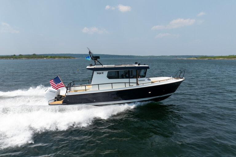 Side view of a Targa 32 Outboard cruising in Casco Bay, Maine, showing the full boat, twin Mercury 350 outboards, and an American flag flying from the stern.