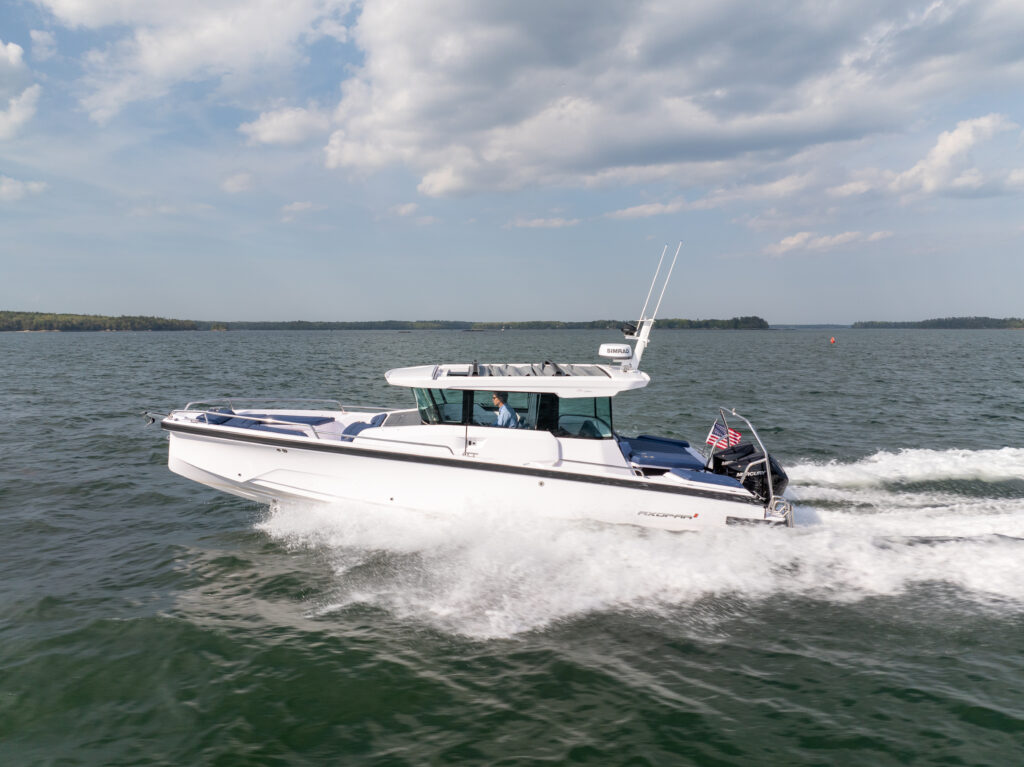 Axopar 29 XC Cross Cabin with a white hull cruising at speed on open water, leaving a foamy wake under a partly cloudy sky.