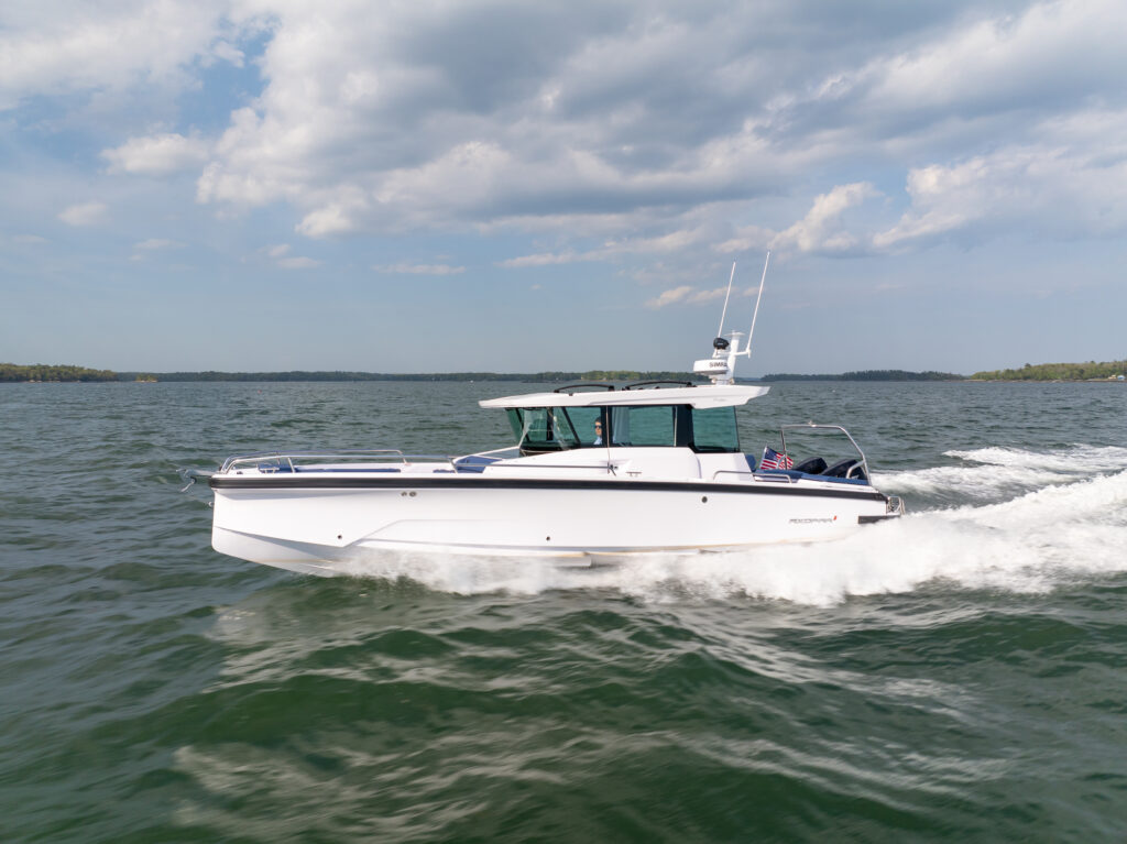 Axopar 29 XC Cross Cabin with a white hull running at speed across choppy water, throwing a white wake under a partly cloudy sky.
