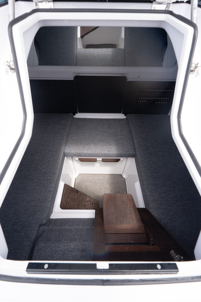 Axopar 29 XC Cross Cabin forward cabin with two long gray berths, a center step/footwell, and a small wood table panel near the entry.
