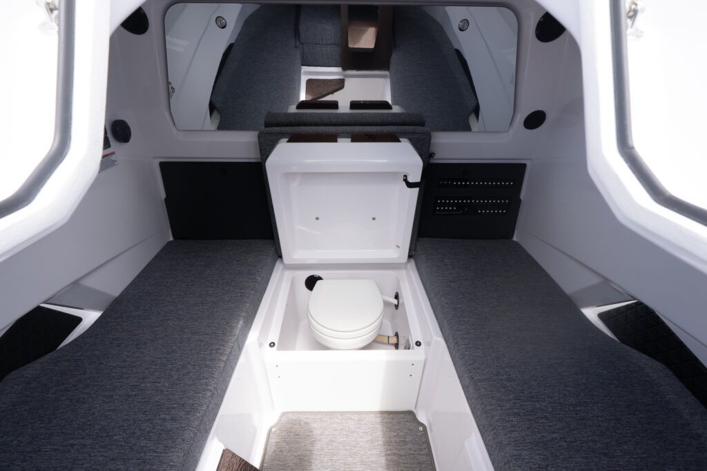 Axopar 29 XC Cross Cabin forward cabin with two long gray berths and a concealed toilet in a central compartment with the lid open.