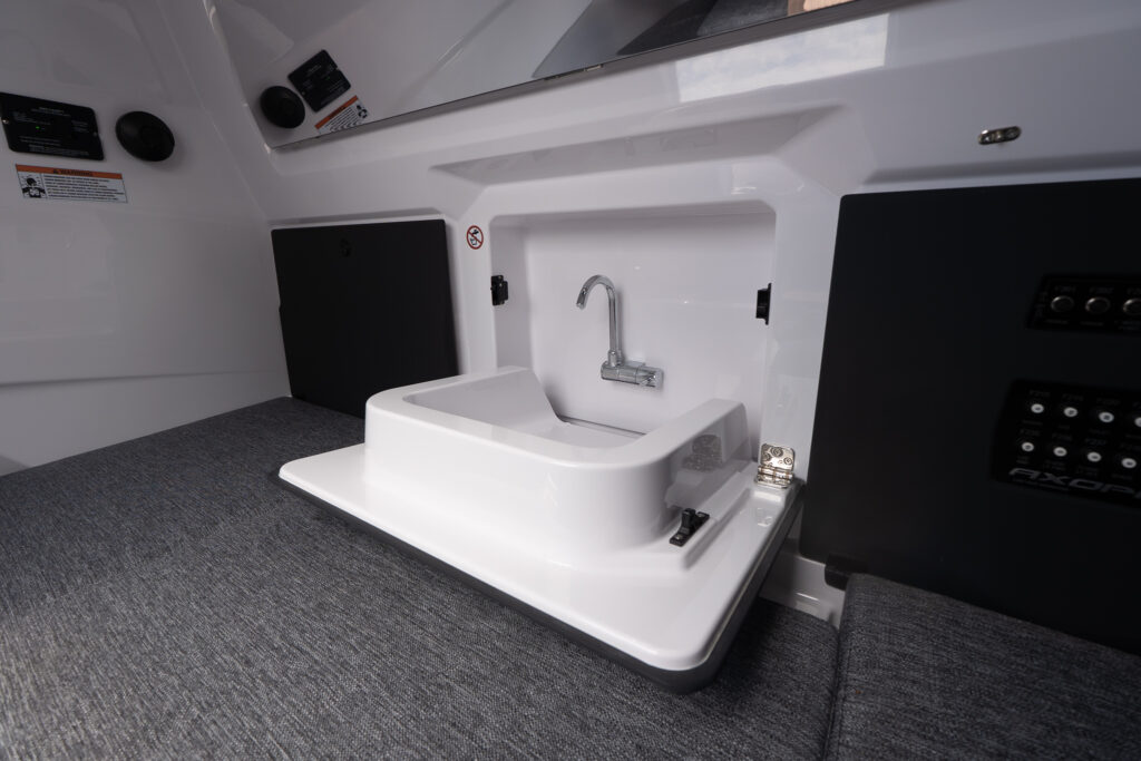 Axopar 29 XC Cross Cabin interior showing a compact sink with faucet mounted on a fold-down countertop between gray cabin cushions and black side panels.