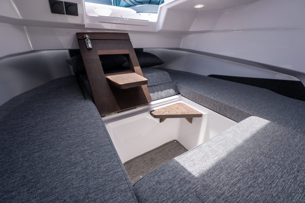Axopar 29 XC Cross Cabin forward cabin with multicabin upgrade, showing split berth cushions arranged around an open center footwell and a hinged wood step/shelf panel.