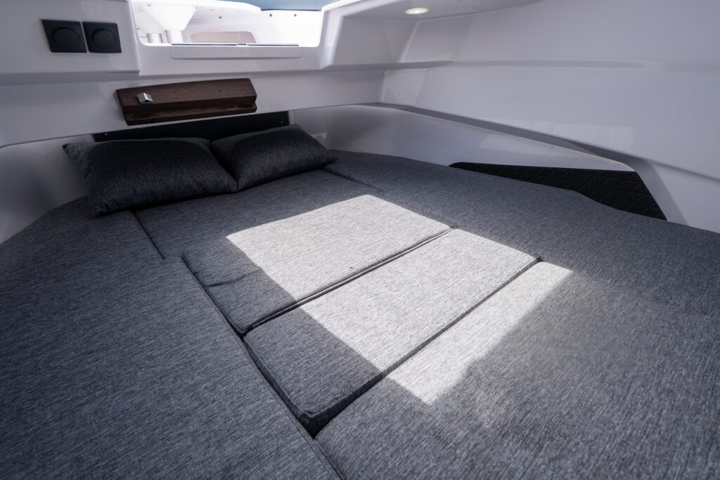 Forward cabin in the Axopar 29 XC Cross Cabin BRABUS Edition with the multicabin upgrade, showing a convertible gray berth with two pillows, side bolsters, and a wood accent shelf.