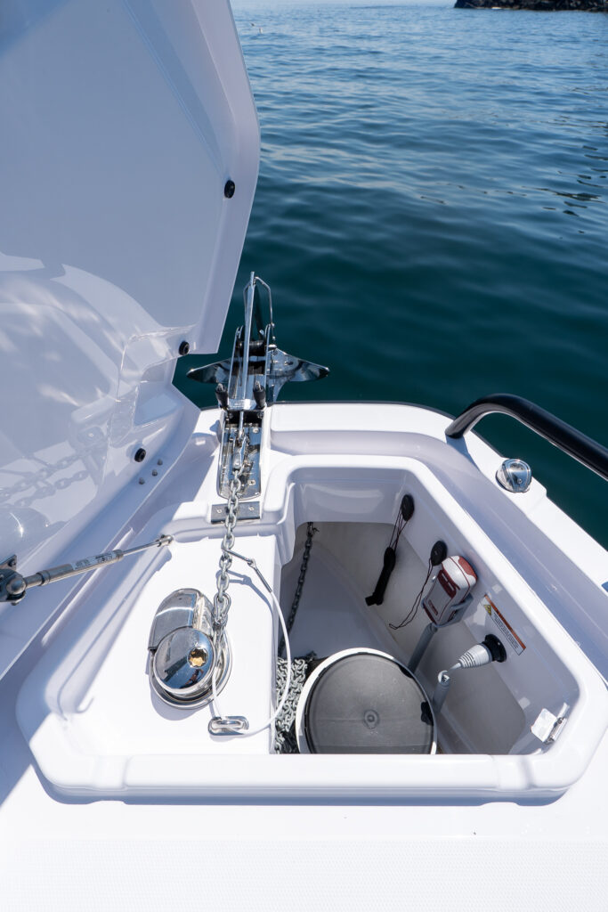 Open anchor locker on an Axopar 29 XC Cross Cabin BRABUS Edition with a stainless anchor on the bow roller, chain, and an electric windlass above the locker.