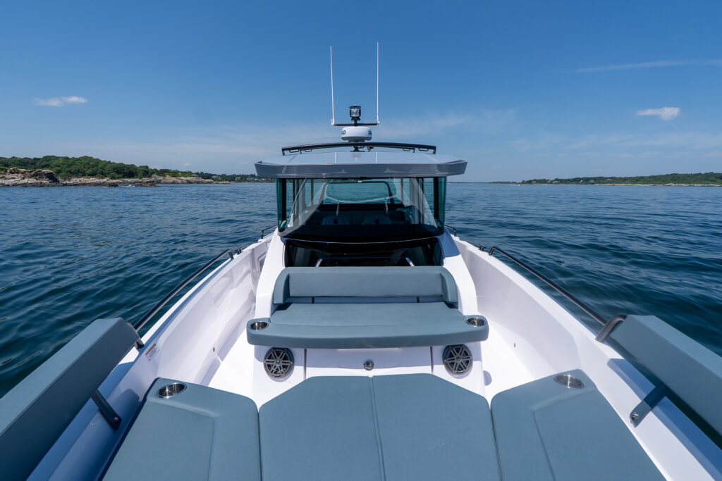 Wide bow view on an Axopar 29 XC Cross Cabin BRABUS Edition showing Petrol-upholstered foredeck seating and sun pad with the Cross Cabin windshield ahead on calm water.