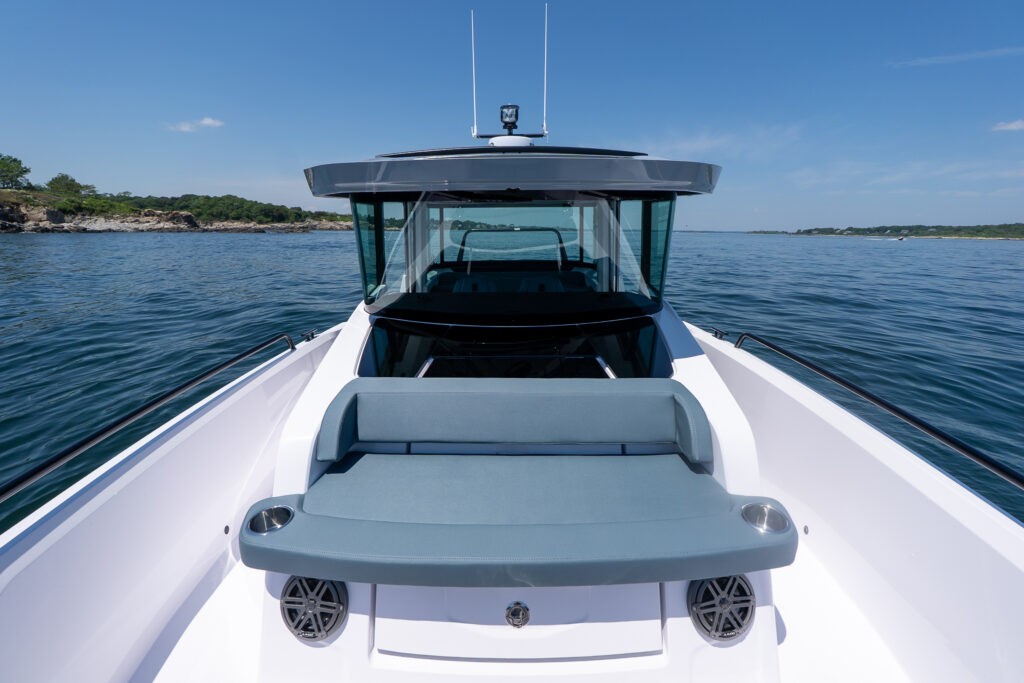 Front-facing view over the Axopar 29 XC Cross Cabin BRABUS Edition foredeck, showing the Petrol-upholstered sun pad and cabin glass on calm water.