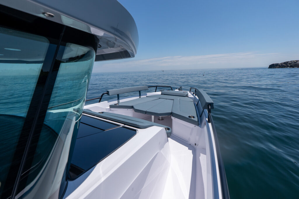 Bow view of an Axopar 29 XC Cross Cabin BRABUS Edition showing the front sun lounge cushions and wraparound seating on calm open water.