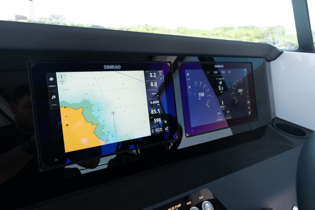 Close-up of two Simrad helm displays on the dashboard of an Axopar 29 XC Cross Cabin, with the left screen showing a nautical chart and the right screen showing engine and system gauge readouts.