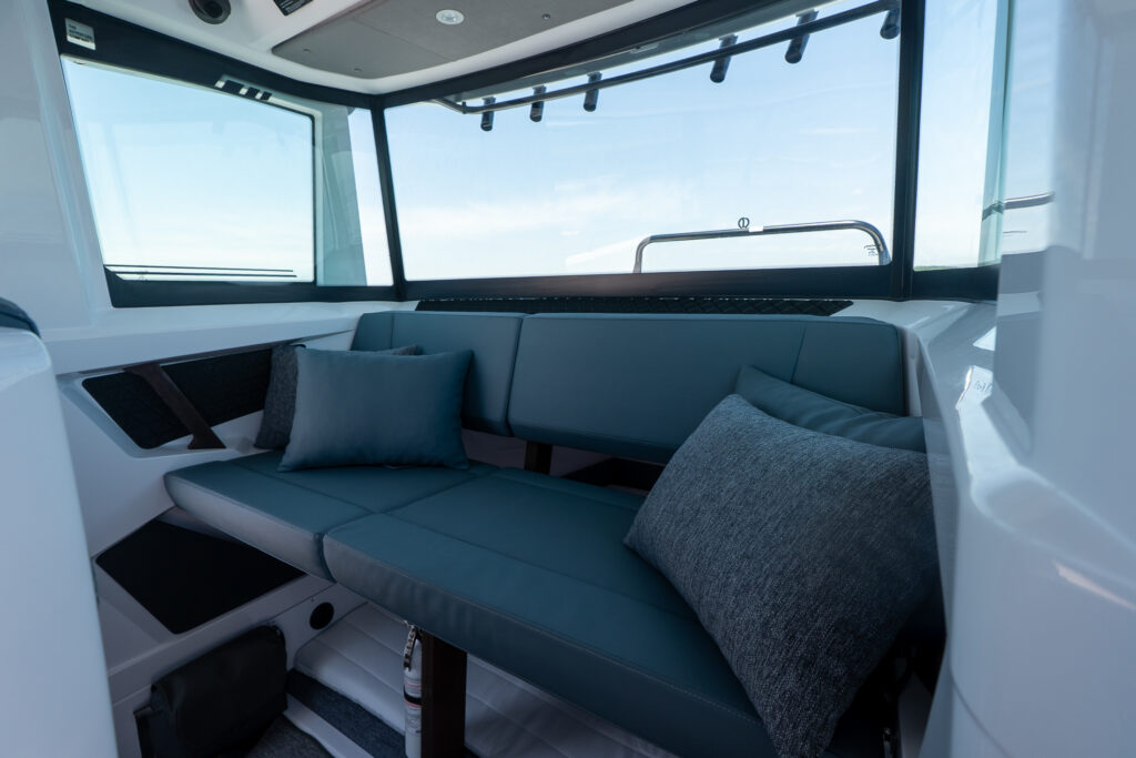 Pilot house aft bench in Petrol upholstery with two throw pillows, wraparound windows, and an open under-seat access hatch leading down toward the aft cabin.