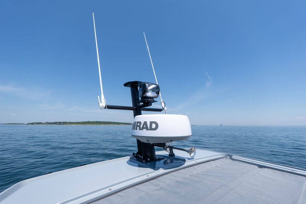 Close-up of a roof-mounted Simrad radar dome with twin VHF antennas and a spotlight above on a black BRABUS edition mast, set against calm open water and a clear blue sky.