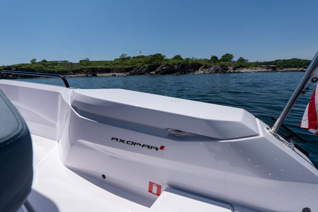 Closed fender locker on an Axopar 29 XC Cross Cabin, with the Axopar logo visible and a rocky Maine shoreline in the background.