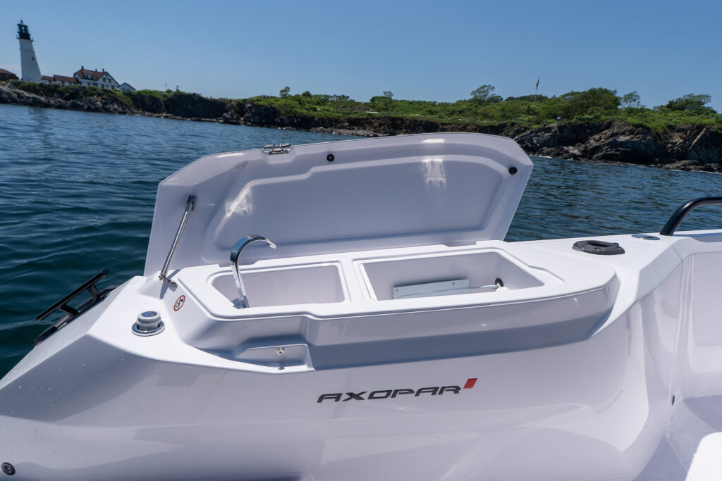 Open fender locker wet bar on an Axopar with a stainless sink and faucet on the left and a built-in fridge compartment on the right, with Portland Head Light in the background.