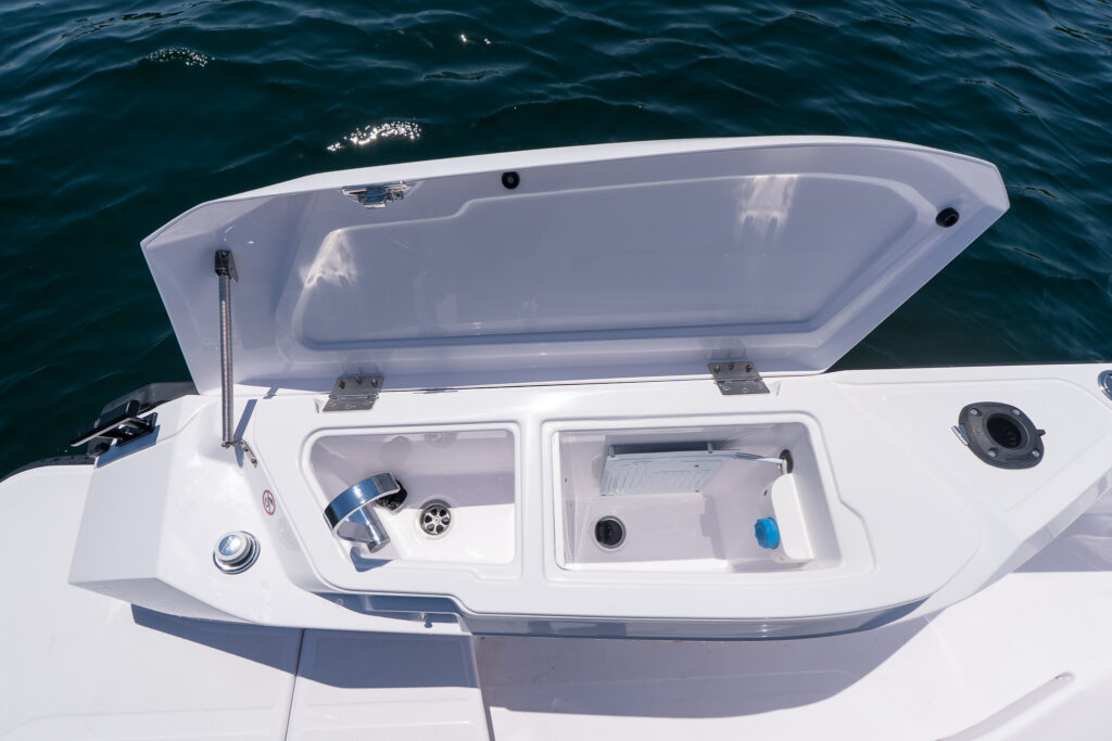 Open fender locker wet bar on an Axopar 29 XC Cross Cabin with a stainless sink and faucet on the left and a built-in fridge on the right, set beside the water.