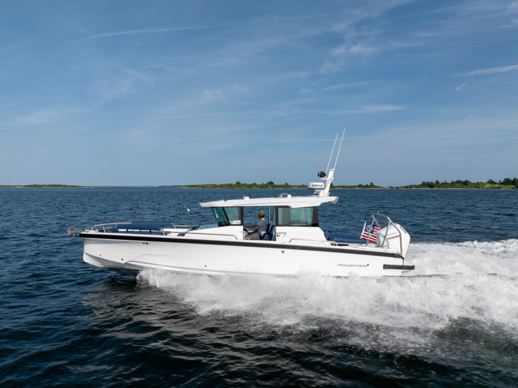 Axopar 29 XC Cross Cabin cruising at speed in Casco Bay, Maine, with Sphere upholstery visible on deck and a single Mercury V10 Verado powering the boat.