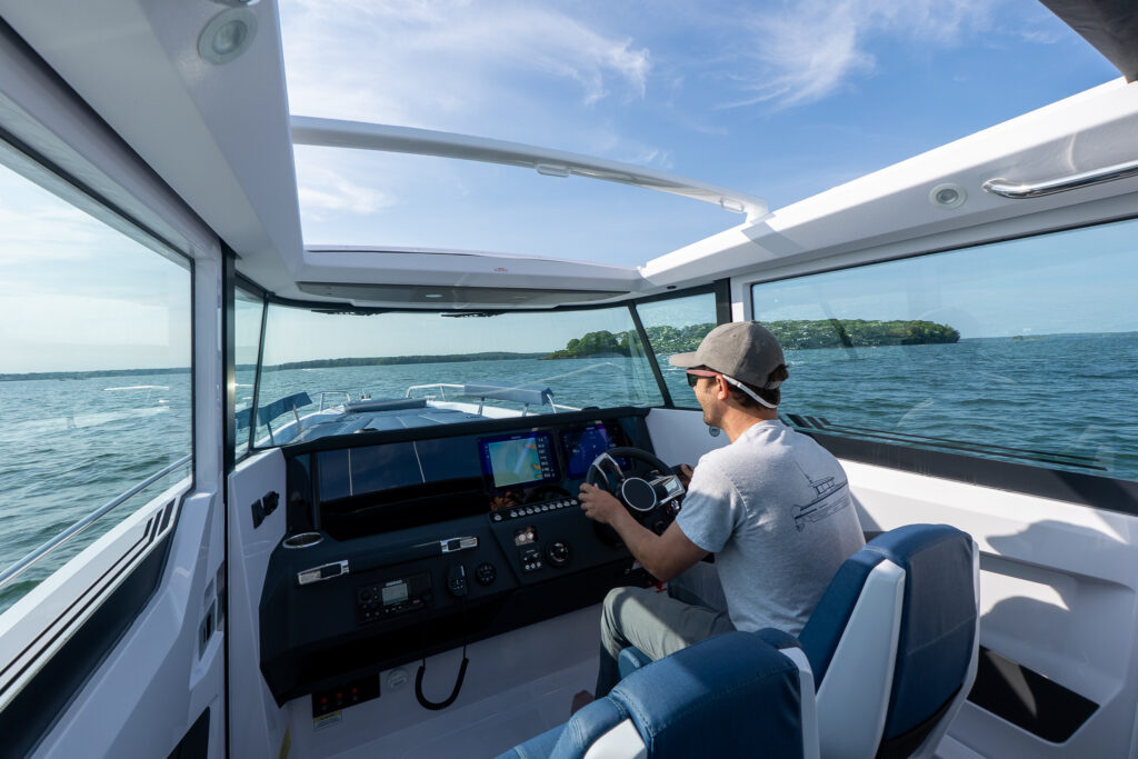 Person driving an Axopar 29 XC Cross Cabin with the roof hatches open, showing the helm, dual displays, and wide visibility over the water.