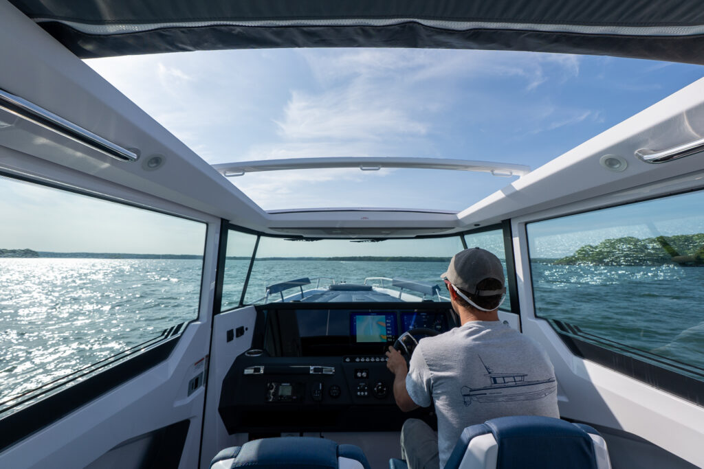 Helm view from inside an Axopar 29 XC Cross Cabin, showing a person driving with the roof hatches open and expansive visibility over the water.