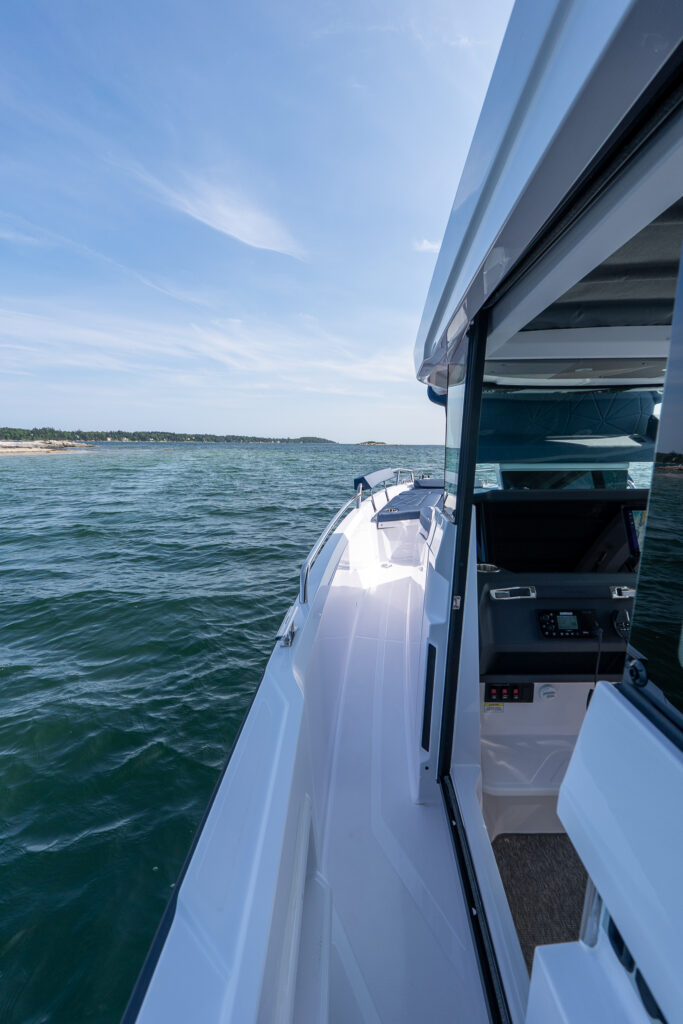 Side deck of an Axopar 29 XC Cross Cabin, showing the pilothouse door open and bow seating visible while cruising in Casco Bay, Maine.