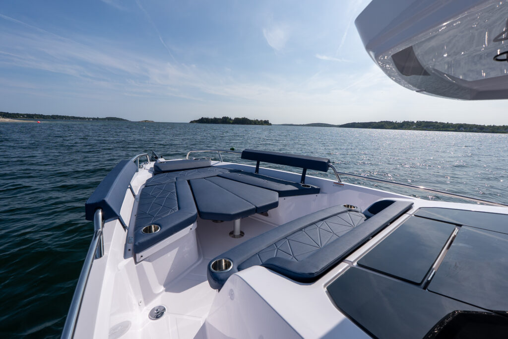 Bow seating area of an Axopar 29 with Sphere blue cushions arranged around a center table while anchored in Casco Bay, Maine on a sunny day.
