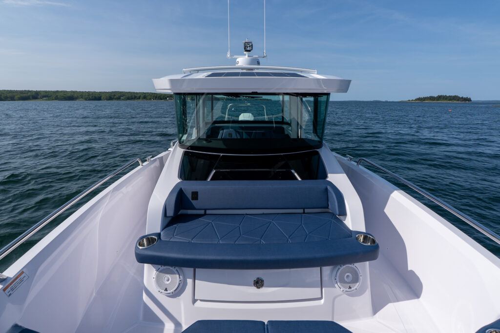 Bow seating area of an Axopar 29 XC Cross Cabin with blue cushions, showing the pilot house and surrounding water in Casco Bay, Maine.