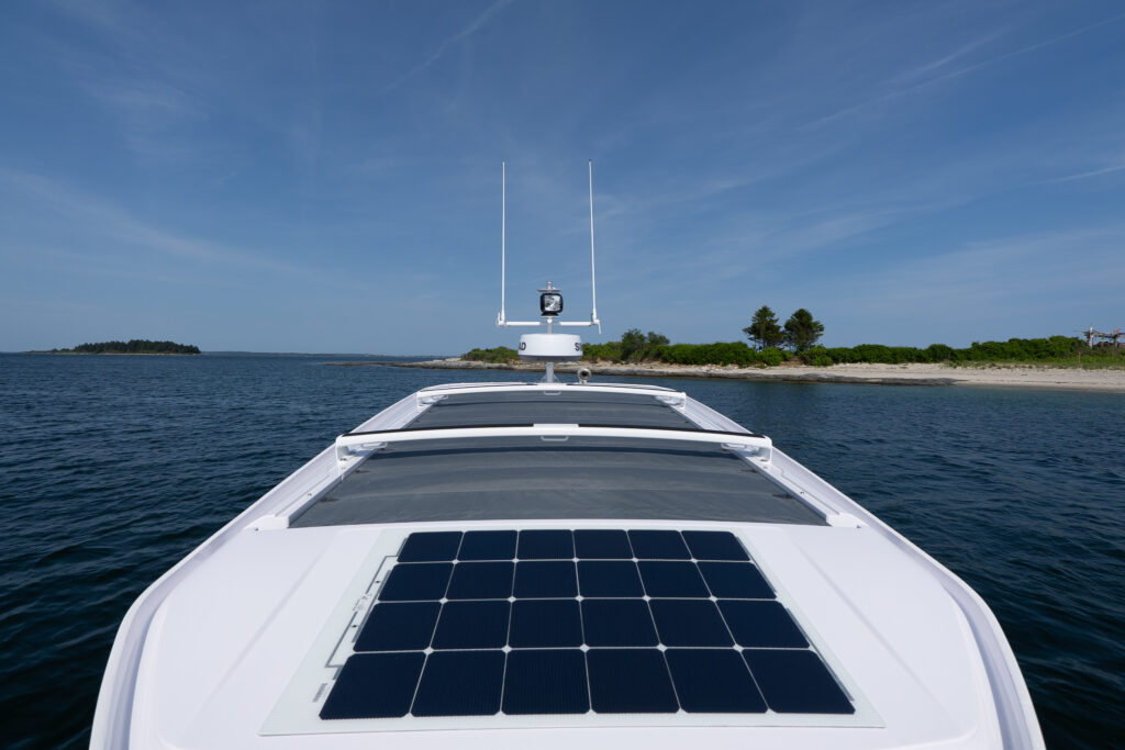View from the bow of an Axopar 29 showing rooftop solar panels and antennas while anchored near a sandy shoreline in Casco Bay, Maine on a clear summer day.
