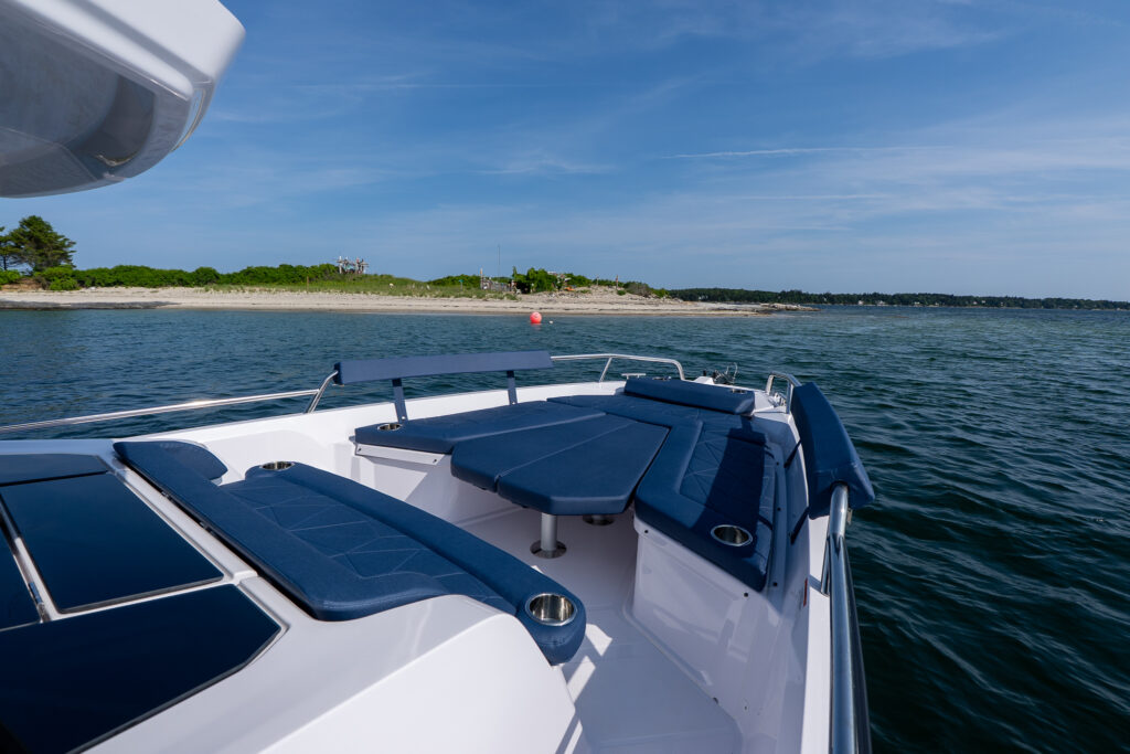 Bow seating of an Axopar 29 with Sphere blue cushions, anchored in Casco Bay, Maine near a sandy shoreline on a sunny day.