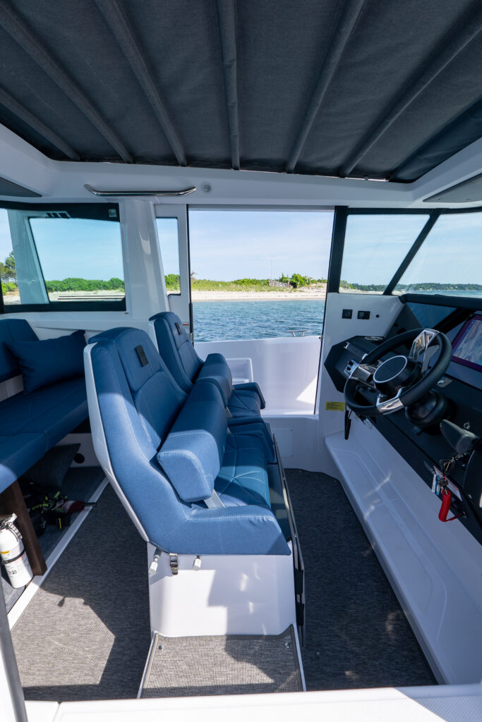 Side view looking port through the Axopar 29 Stock 34 cabin showing cockpit, captain’s seats with Sphere upholstery, and aft bench with Casco Bay and islands in the background