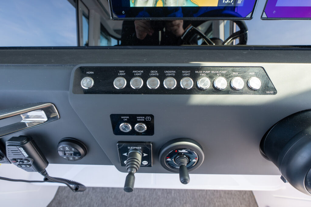 Close-up of Axopar 29 Stock 34 helm dashboard showing controls for radio, navigation lights, bow thruster, bilge pumps, trim tabs, and windshield wipers