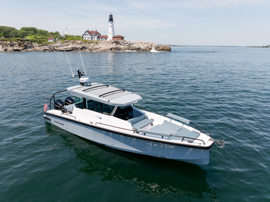 Aerial view of a BRABUS edition Axopar 29 XC Cross Cabin on calm water with Portland Head Light and the rocky Maine coastline in the background.