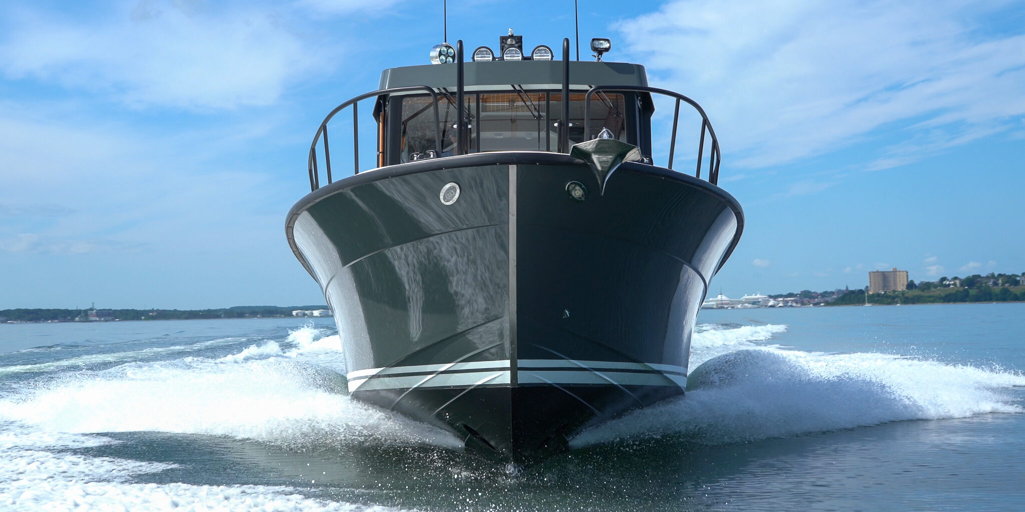 Targa 32 with green hull cruising head-on in Casco Bay, Portland, Maine, with the Eastern Promenade visible in the distance.