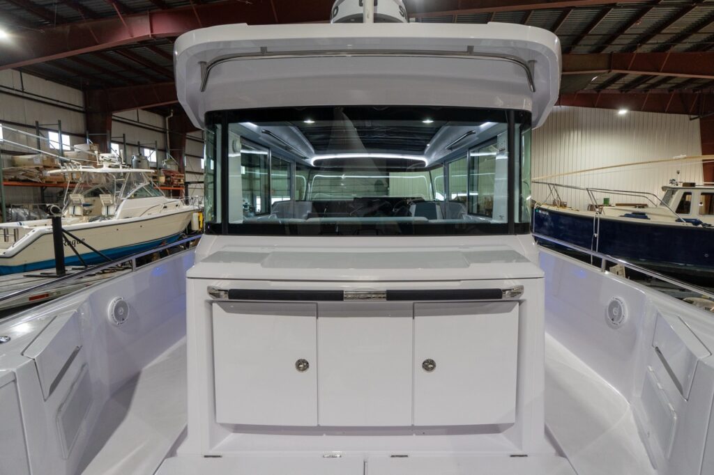Straight-on view of the Axopar 37 XC aft wet bar module on the aft deck, showing a wide countertop and double-door storage cabinet beneath the pilothouse’s full-width rear window, with open side decks running along both sides.