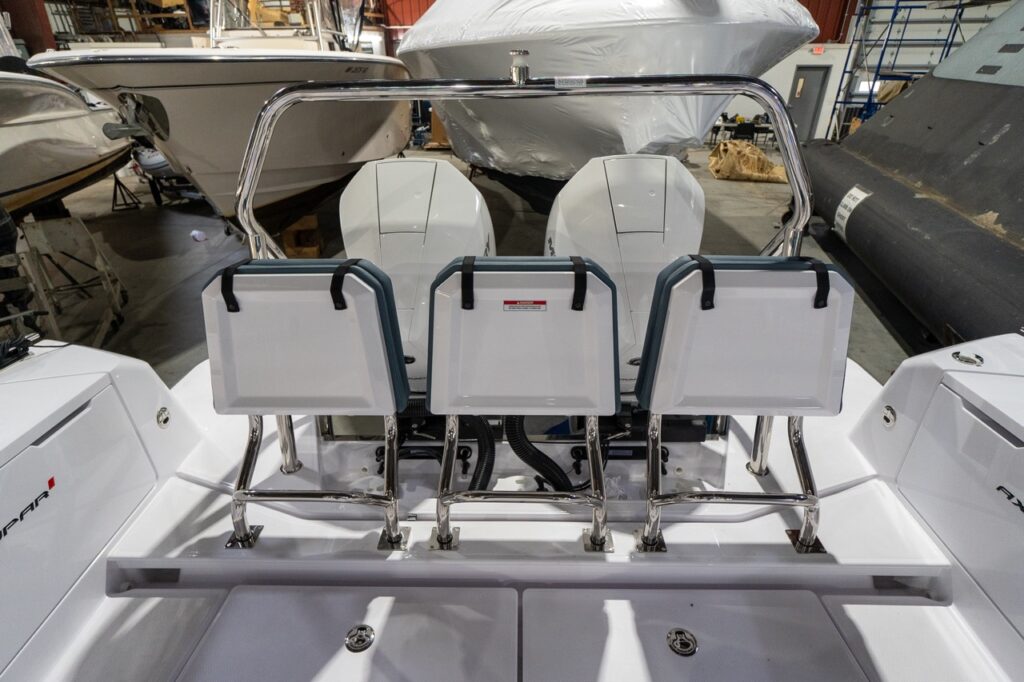 Aft deck view on an Axopar 37 XC with the three petrol-upholstered staple seats folded up and stowed vertically, opening up the deck area in front of the twin outboard engines and stainless grab rail.