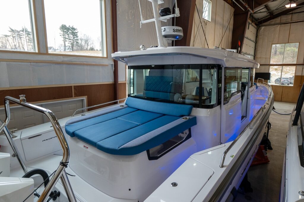 Axopar 37 XC Cross Cabin in an indoor showroom featuring a Baltic blue Sun bed and wraparound cabin windows.