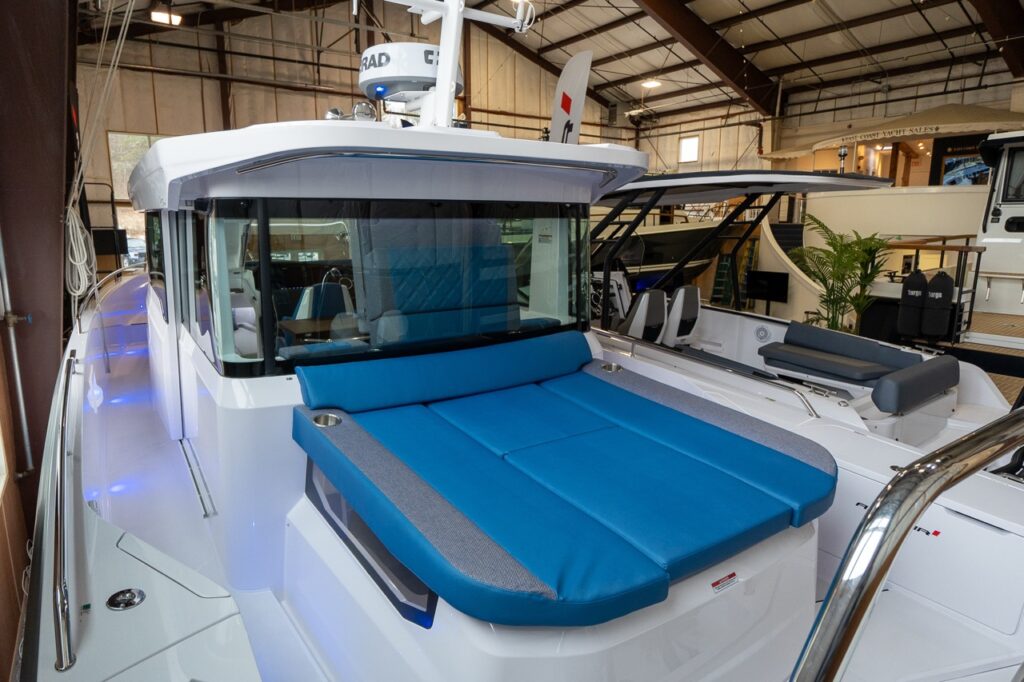 Axopar 37 XC Cross Cabin photographed in an indoor showroom with the aft deck sunpad fitted in Baltic blue upholstery and integrated cupholders.