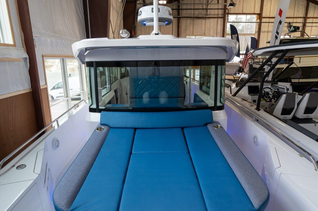 Rear-facing view in an indoor showroom of an Axopar 37 XC Cross Cabin with the aft deck sunpad in Baltic blue upholstery and grey side bolsters with cupholders.
