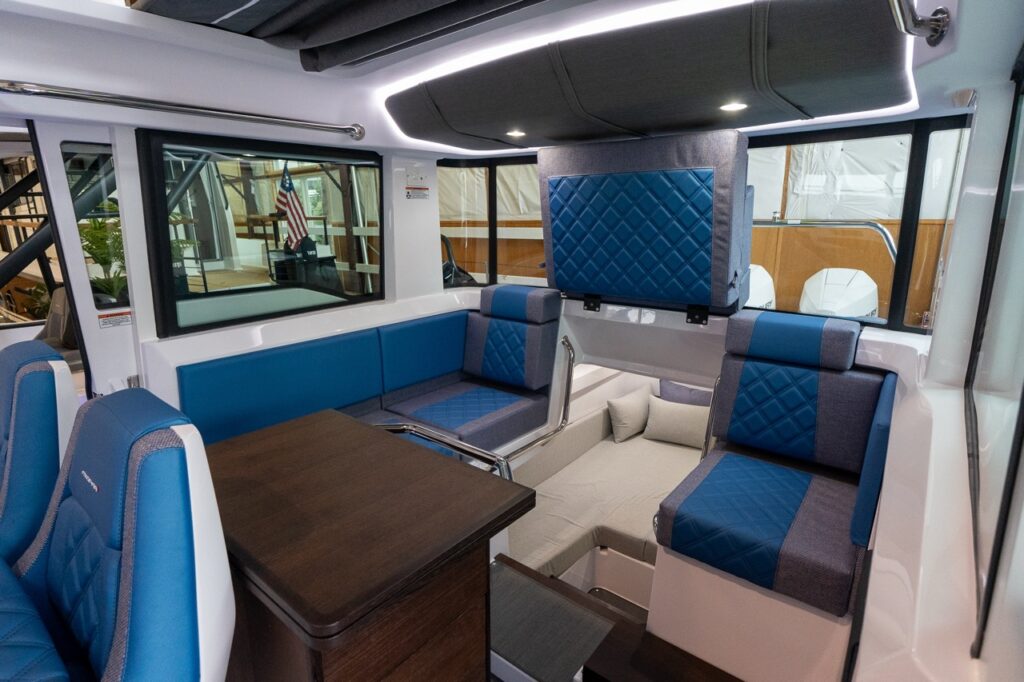 Axopar 37 XC pilot house interior looking aft, showing Baltic blue diamond-stitched seats, galley module, and the aft cabin entrance with steps down.