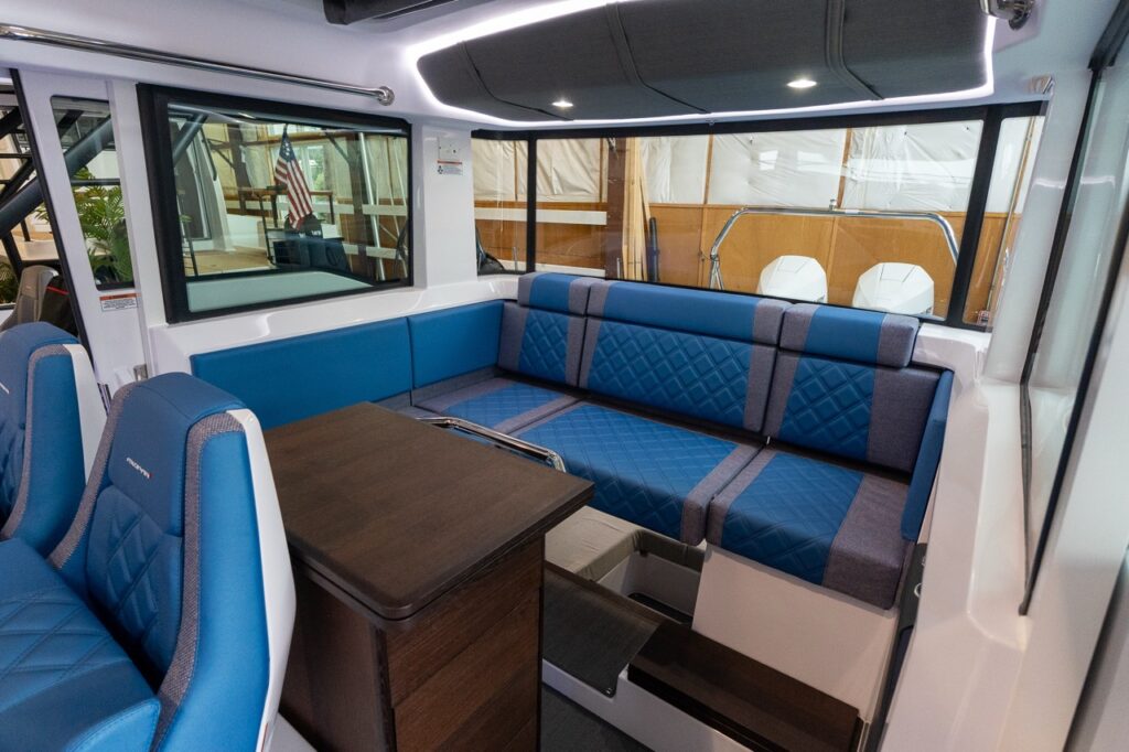 Axopar 37 XC pilot house lounge with Baltic blue diamond-stitched seating, wood table, cabin steps, and wide aft windows.