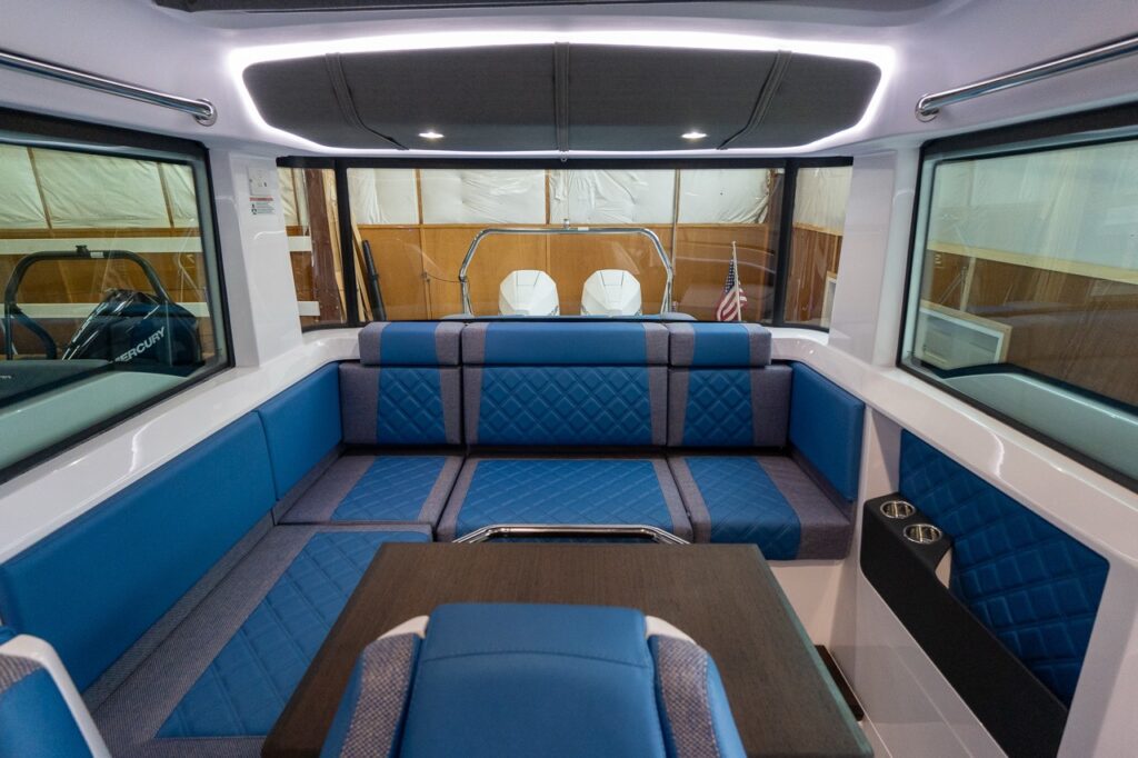 Axopar 37 XC pilot house aft lounge with Baltic blue diamond-stitched seating, wood table, cupholders, and panoramic windows.