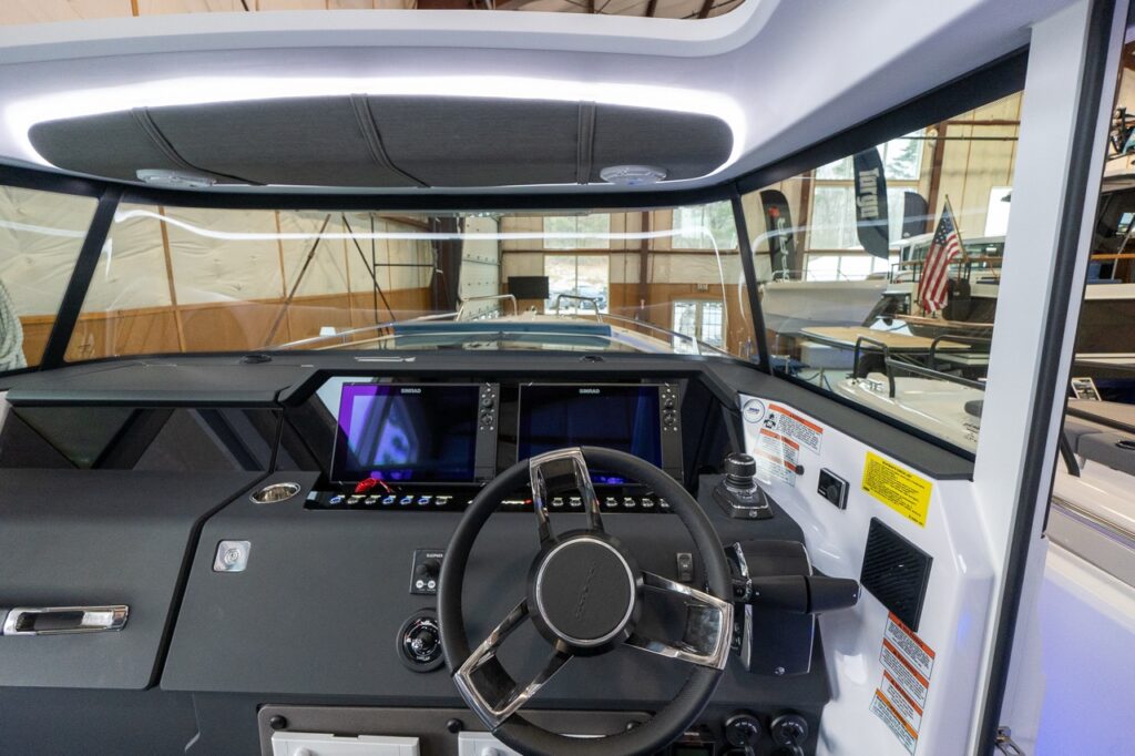Axopar 37 XC Cross Cabin helm station with steering wheel, dual Simrad navigation screens, throttle controls, and wraparound windshield in the pilot house.