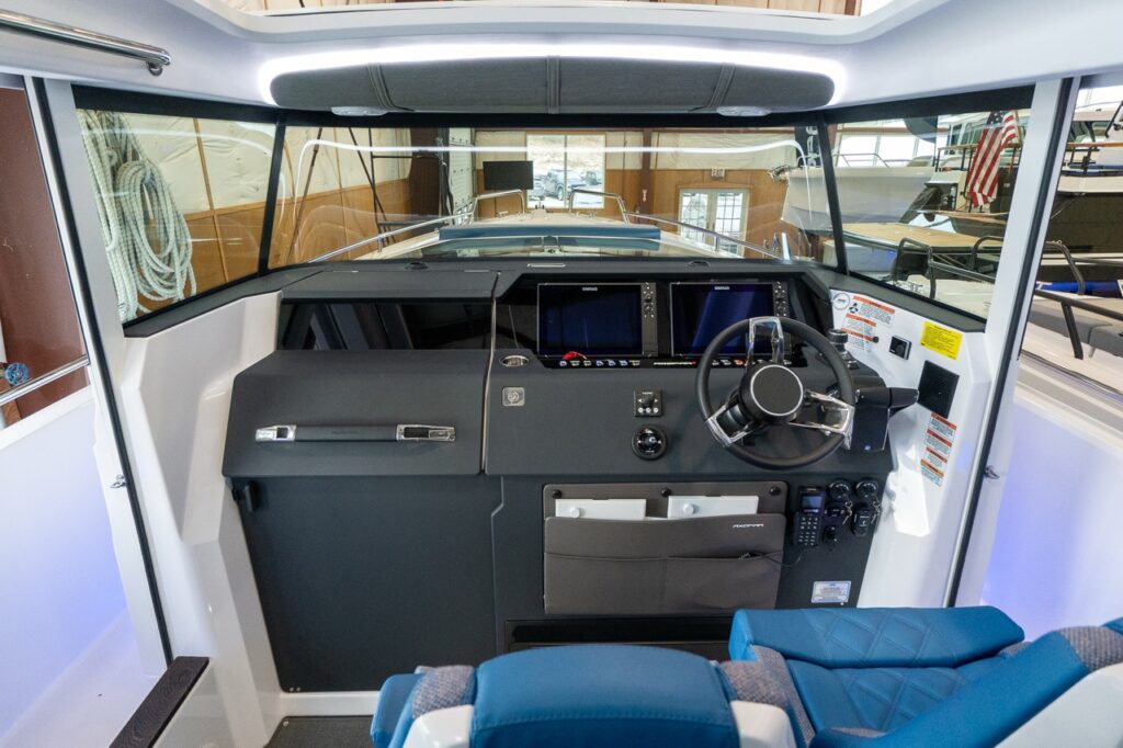 Wide view of the Axopar 37 XC Cross Cabin pilot house helm with steering wheel, dual Simrad displays, glovebox, and wraparound windshield.