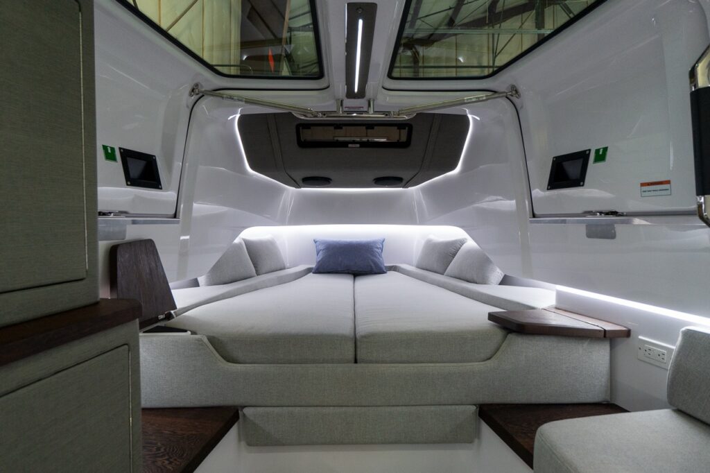 Axopar 37 XC aft cabin double berth with grey cushions, skylights in the closed gullwing doors overhead, and ambient LED lighting.
