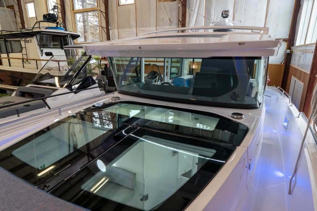 Axopar 37 XC Cross Cabin in an indoor showroom, showing the gullwing doors with integrated roof windows above the forward cabin and the large foredeck glass panels.