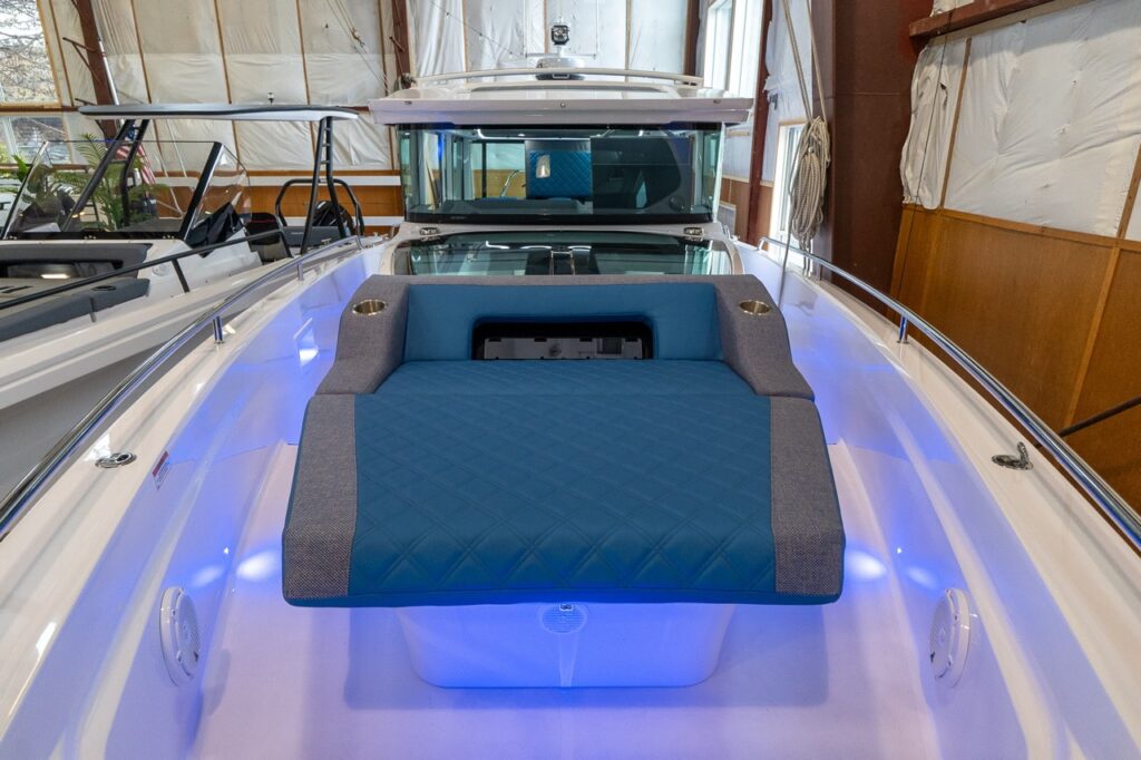 Foredeck sunbed on an Axopar 37 XC Cross Cabin in an indoor showroom, upholstered in Baltic blue with gray bolsters and integrated cupholders.